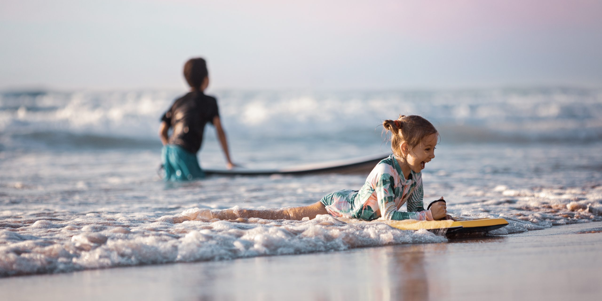 Happy baby girl - young surfer ride on surfboard with fun on sea waves. Active family lifestyle, kids outdoor water sport lessons and swimming activity in surf camp. Summer vacation with child.